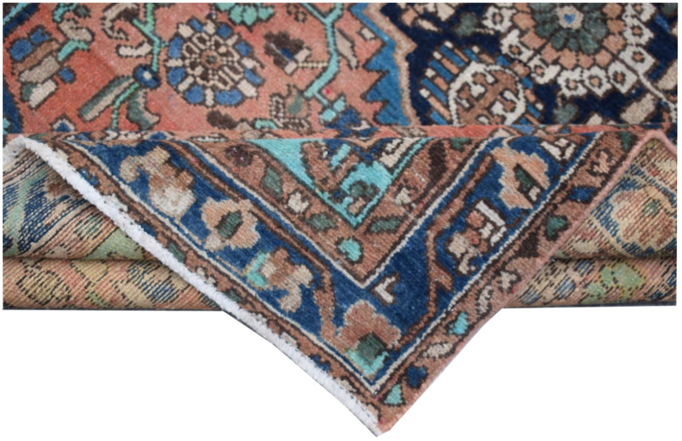 A folded vintage Persian wool rug featuring intricate tribal patterns in blue, pink, and brown.