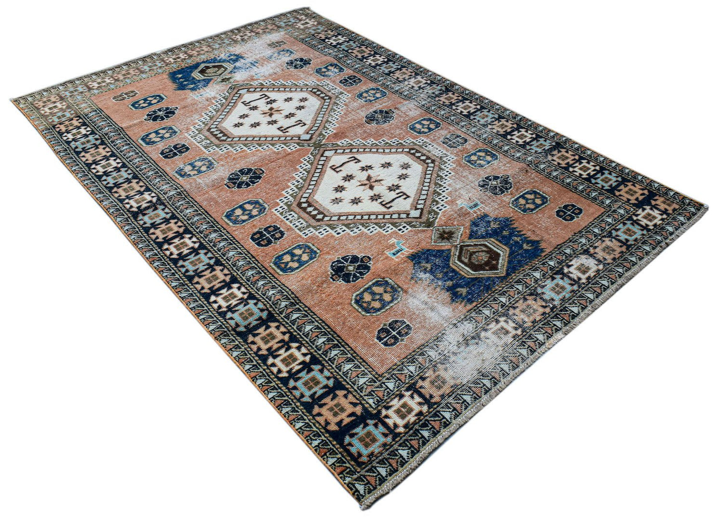 A vintage handwoven Persian rug featuring geometric medallions on a faded terracotta background.
