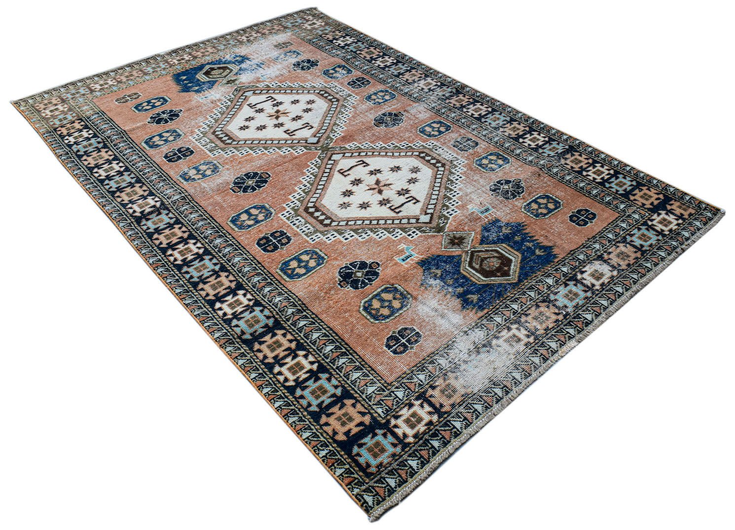 A vintage handwoven Persian rug featuring geometric medallions on a faded terracotta background.