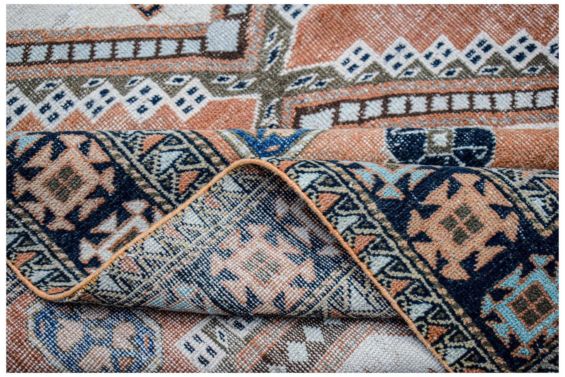 A handwoven vintage Persian rug featuring geometric patterns in shades of orange, blue, and cream.