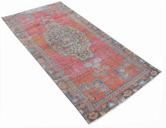 A vintage handwoven Persian rug featuring a faded red and orange floral pattern.