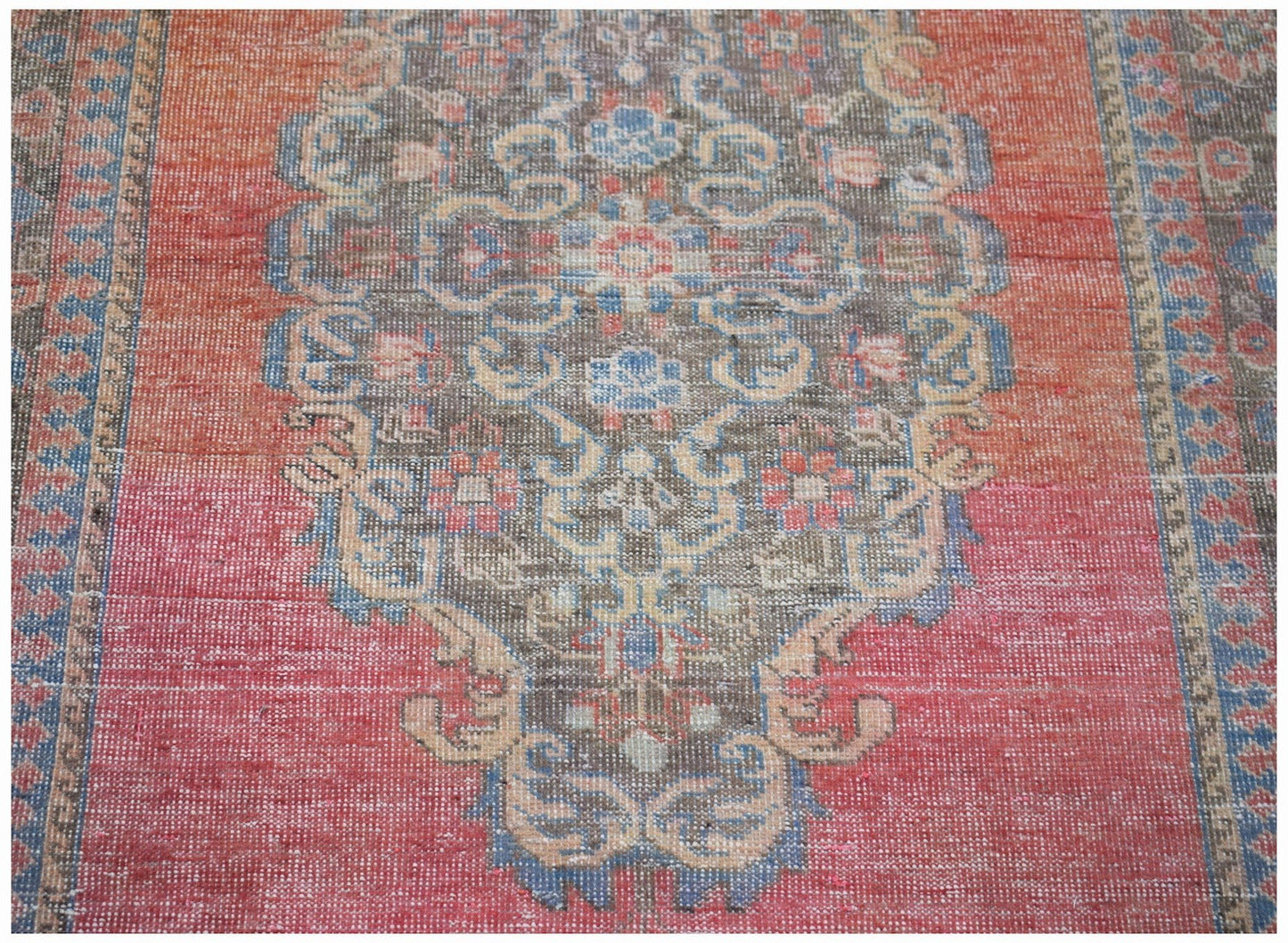 A vintage handwoven Persian rug featuring a central floral medallion on a faded red background.