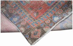 A vintage handwoven Persian rug featuring a floral pattern in faded red, blue, and brown tones.