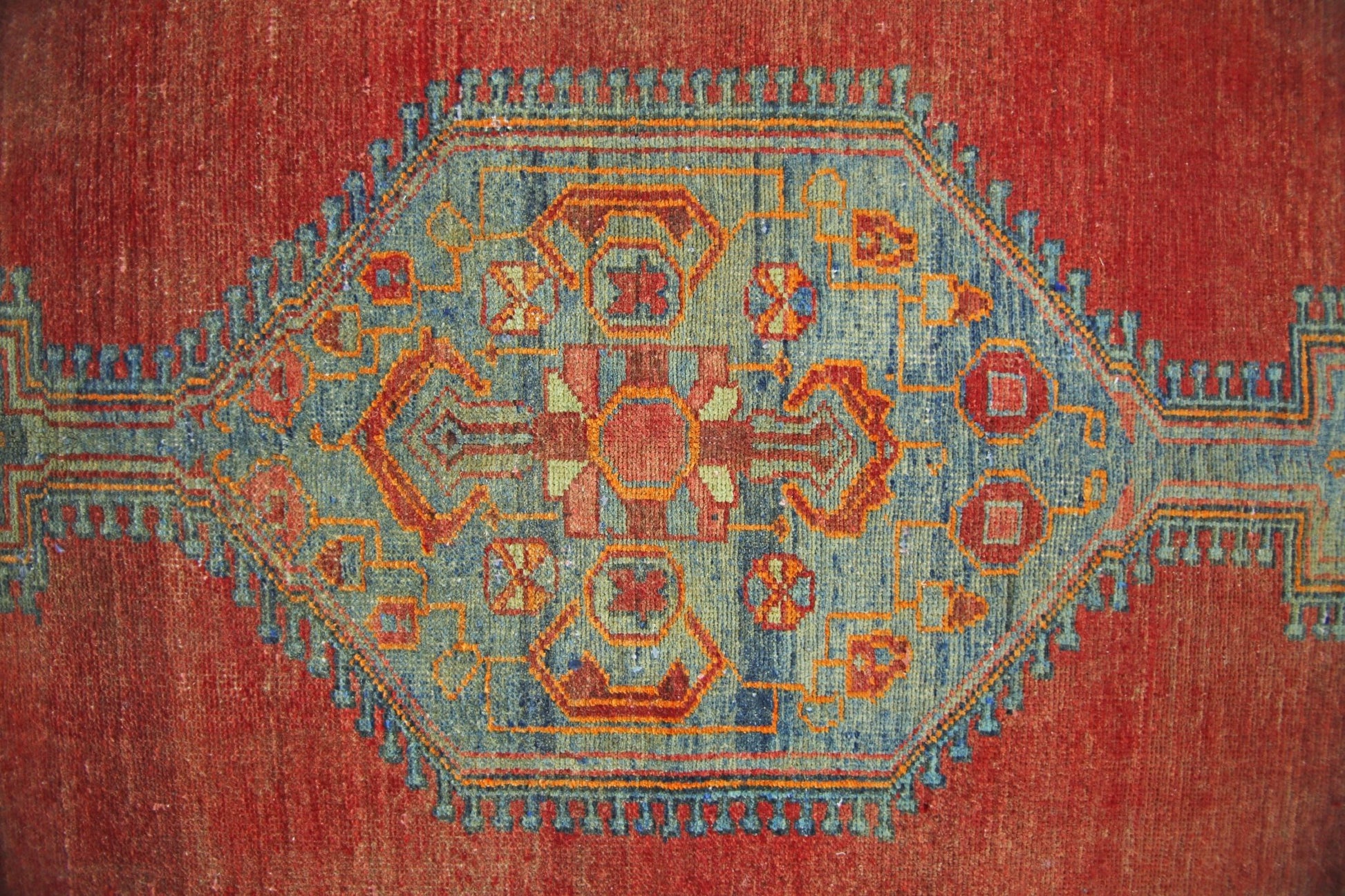 A vintage Persian rug featuring a central blue geometric medallion on a red wool field.