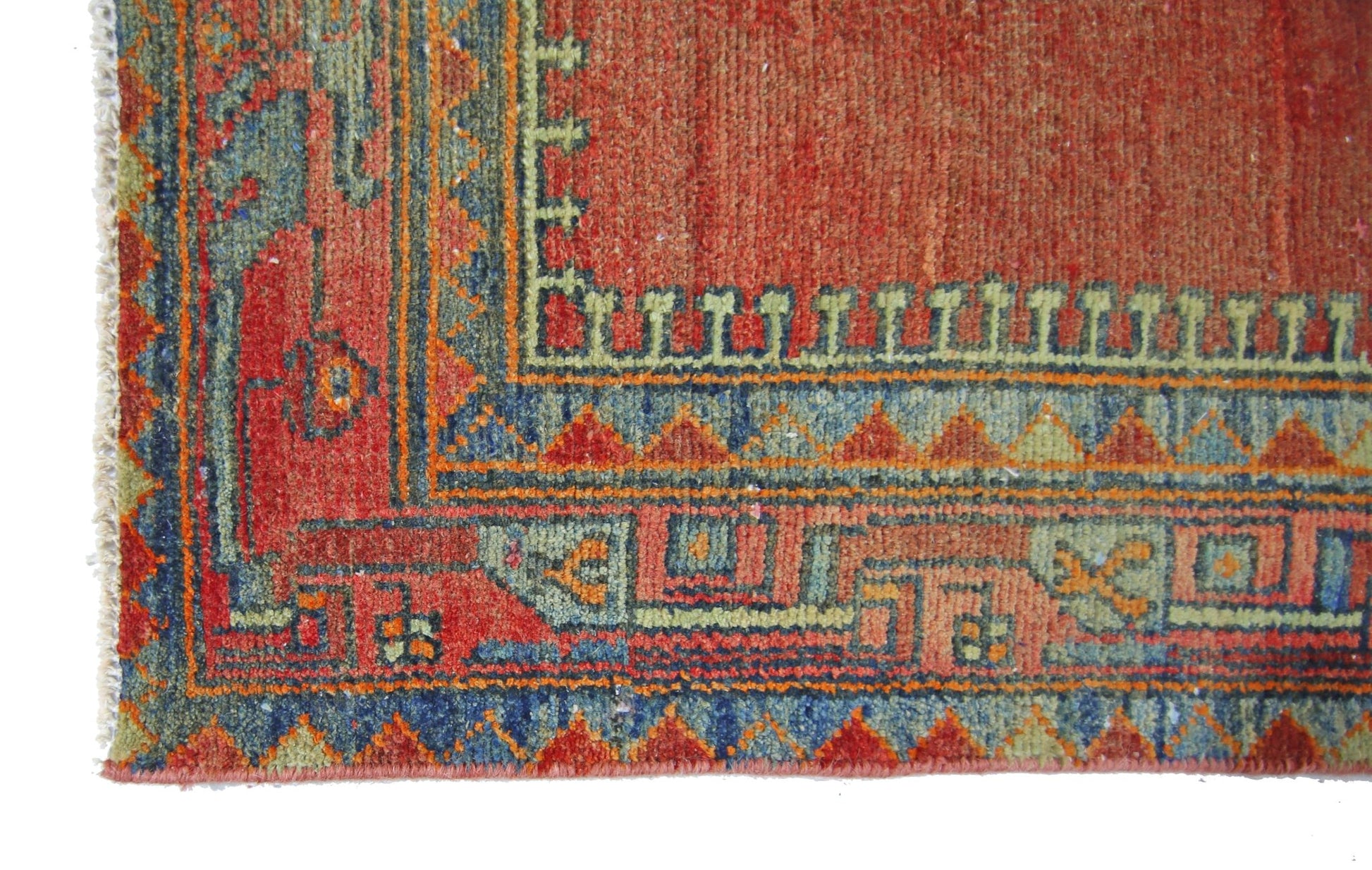 A corner detail of a vintage Persian rug featuring geometric patterns in red, blue, and green.