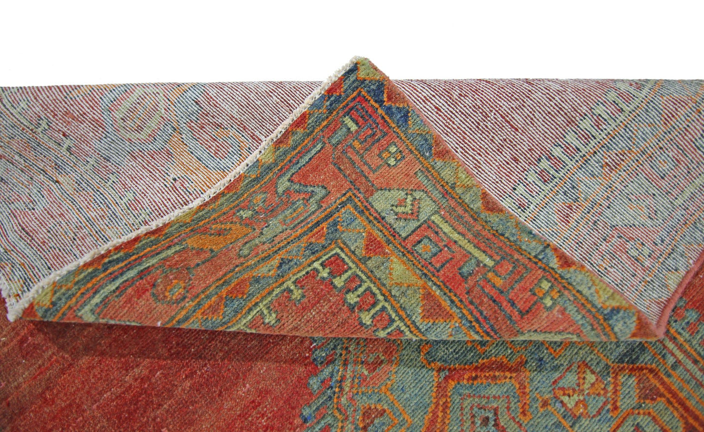 A corner of a vintage Persian rug is folded back to reveal its red, blue, and green geometric design.