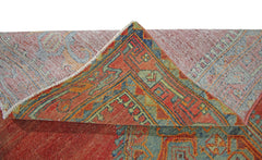 A corner of a vintage Persian rug is folded back to reveal its red, blue, and green geometric design.