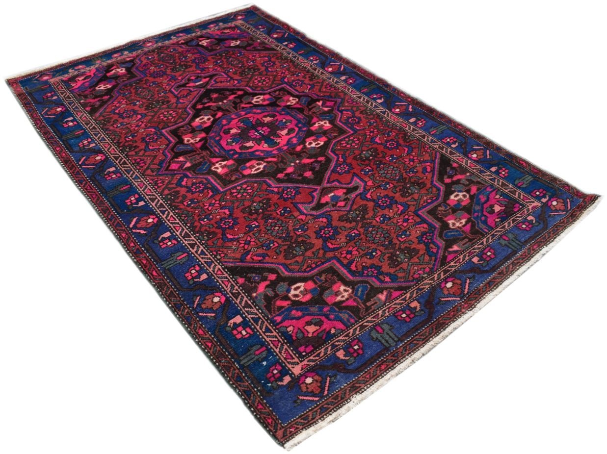 A rectangular vintage Persian rug featuring a central medallion in shades of red, blue, and black.