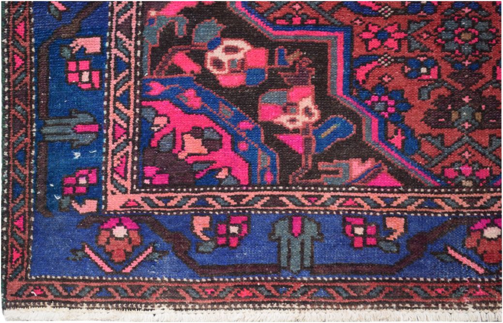 A vintage Persian wool rug featuring a geometric floral pattern in vibrant pink, blue, and black.