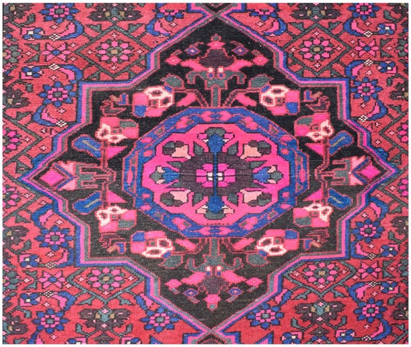 A vintage Persian wool rug featuring a central geometric medallion in vibrant pink and blue tones.