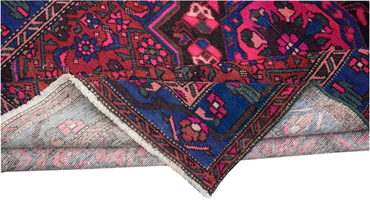 A folded vintage Persian rug featuring intricate tribal patterns in vibrant pink, blue, and red.