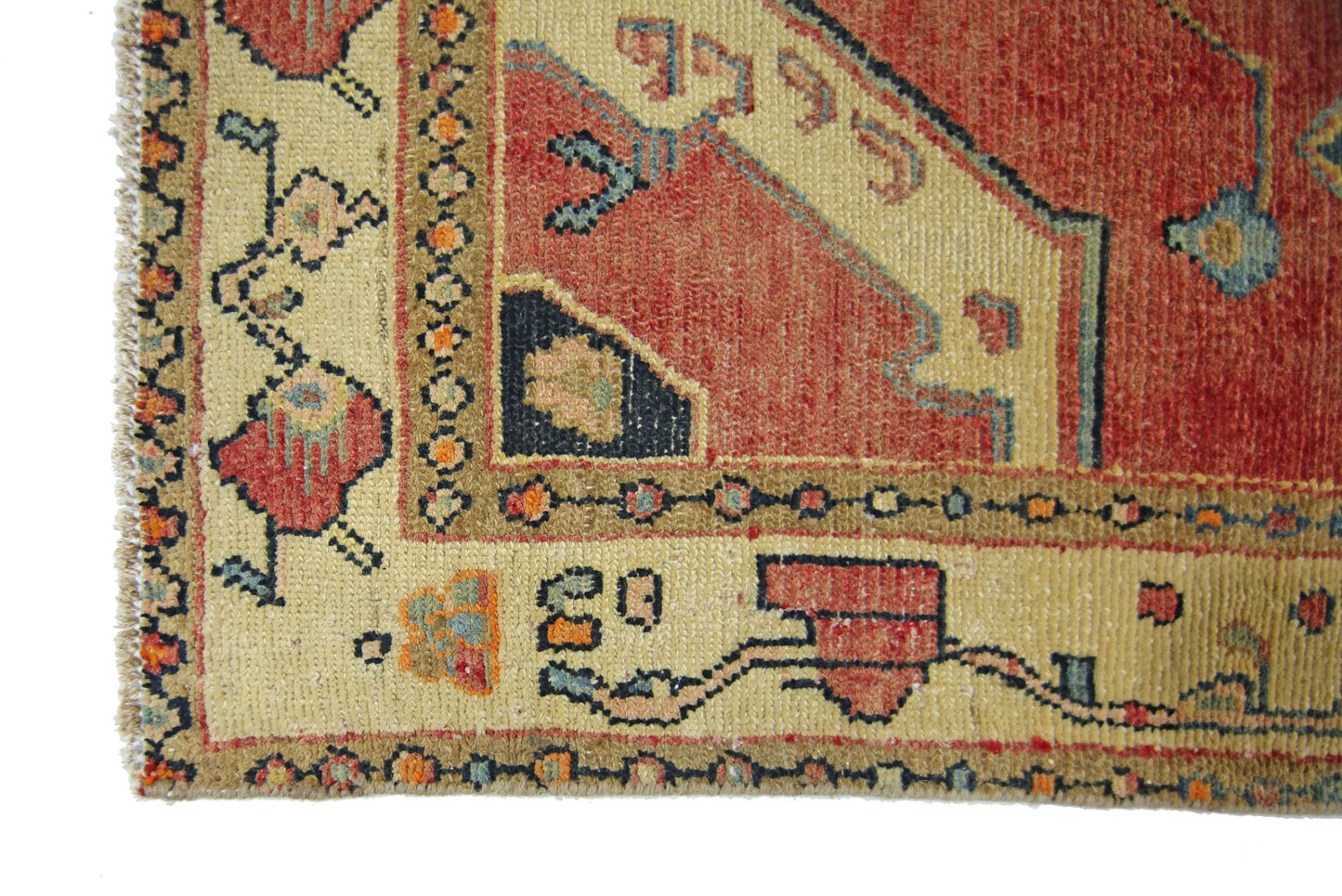 A corner view of a vintage Persian rug featuring geometric patterns in red, beige, and blue.