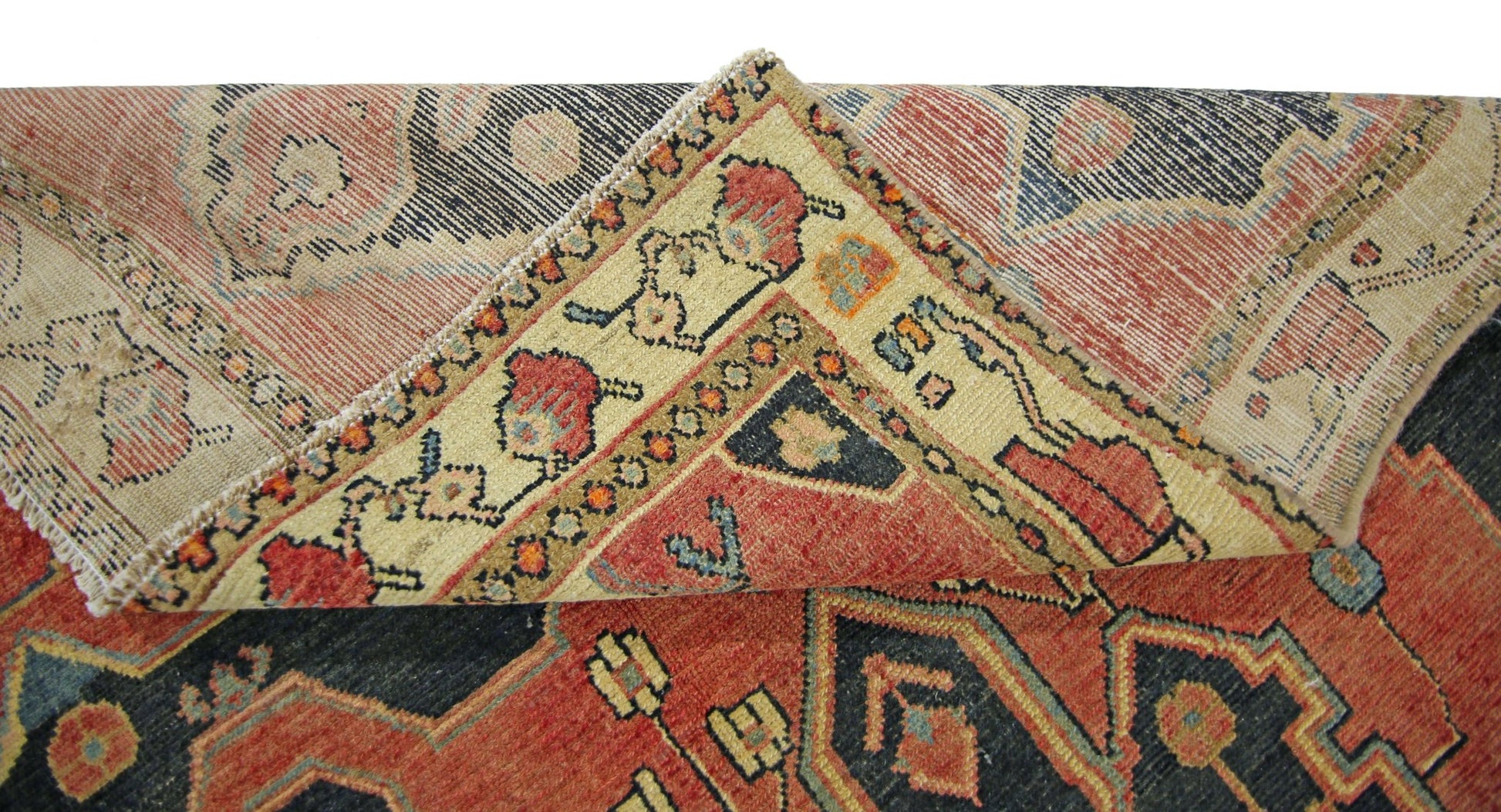 A vintage Persian rug with a folded corner revealing its intricate red and blue geometric pattern.