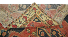 A vintage Persian rug with a folded corner revealing its intricate red and blue geometric pattern.