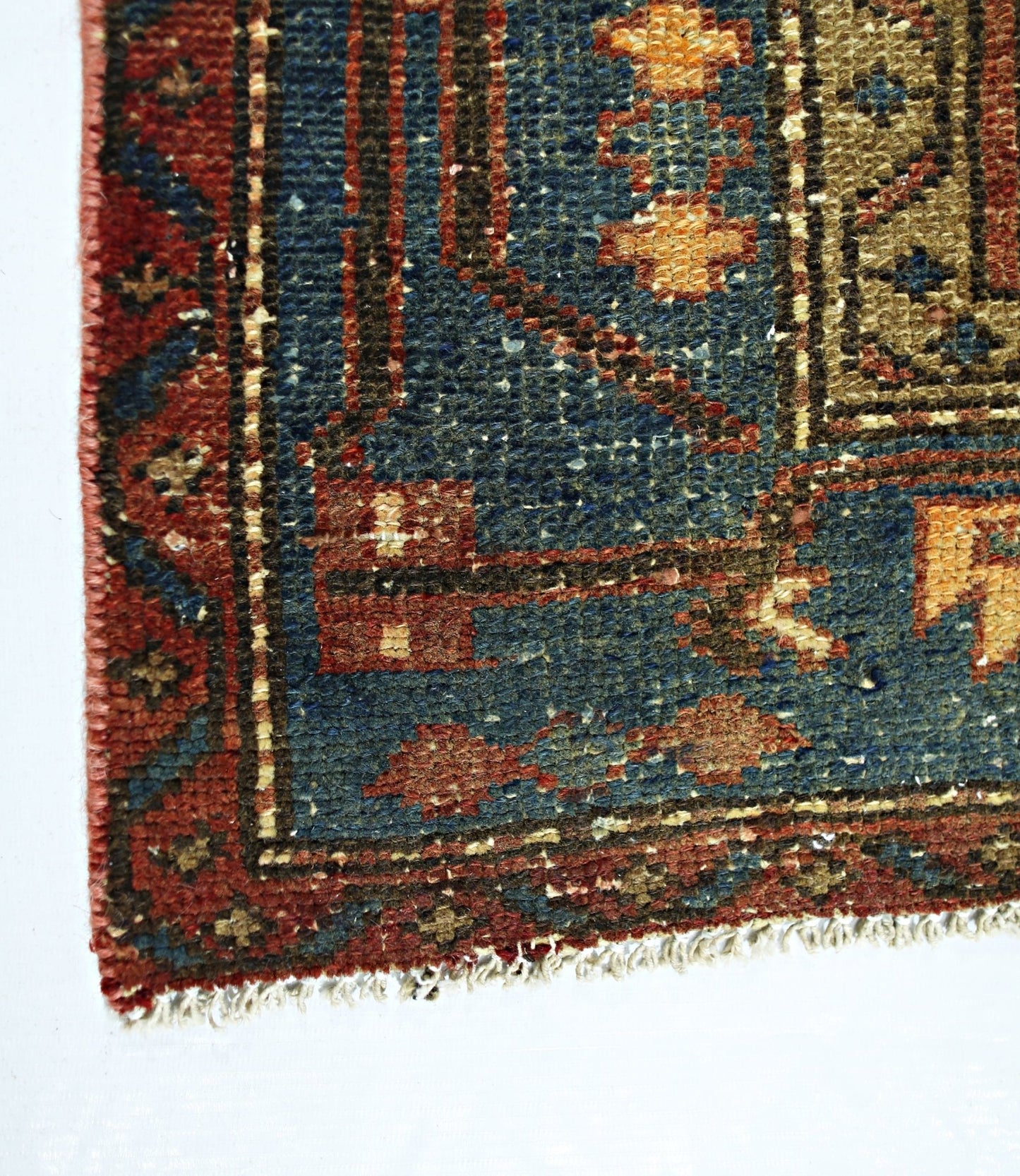 A corner view of a vintage Persian rug featuring a blue field with geometric patterns and red borders.
