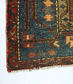A corner view of a vintage Persian rug featuring a blue field with geometric patterns and red borders.