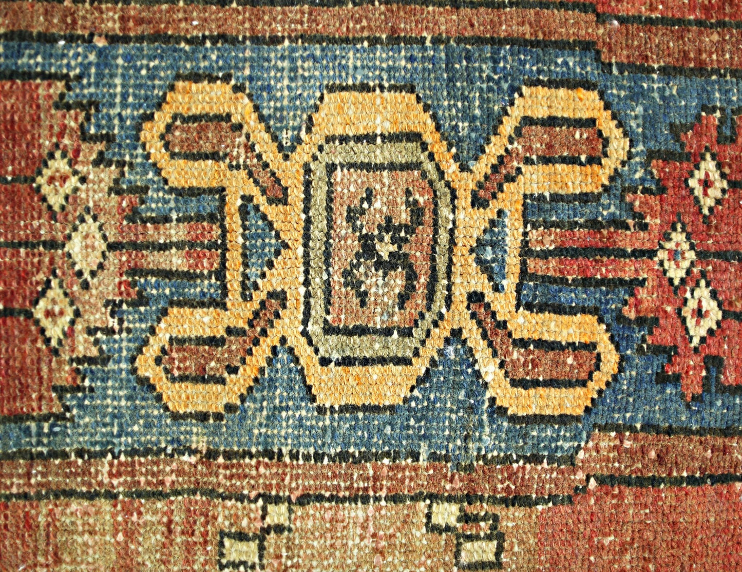 A close-up of a vintage Persian rug featuring a central geometric motif in blue, gold, and red.