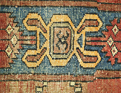 A close-up of a vintage Persian rug featuring a central geometric motif in blue, gold, and red.
