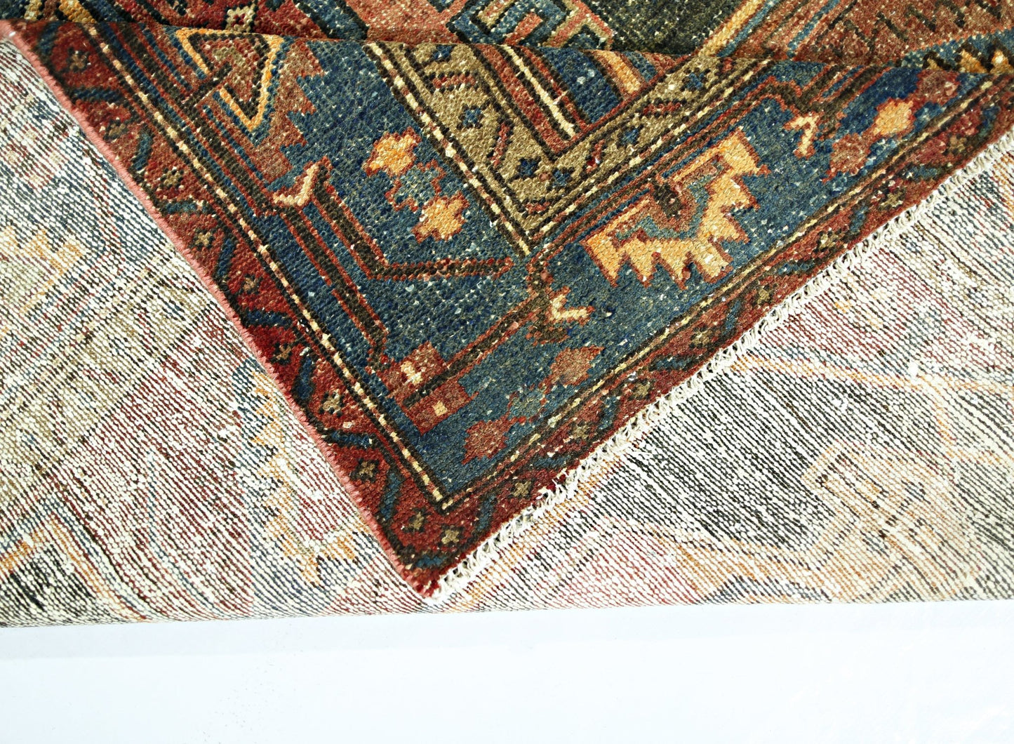 A corner of a vintage Persian rug is folded over to show its intricate blue and red wool pattern.