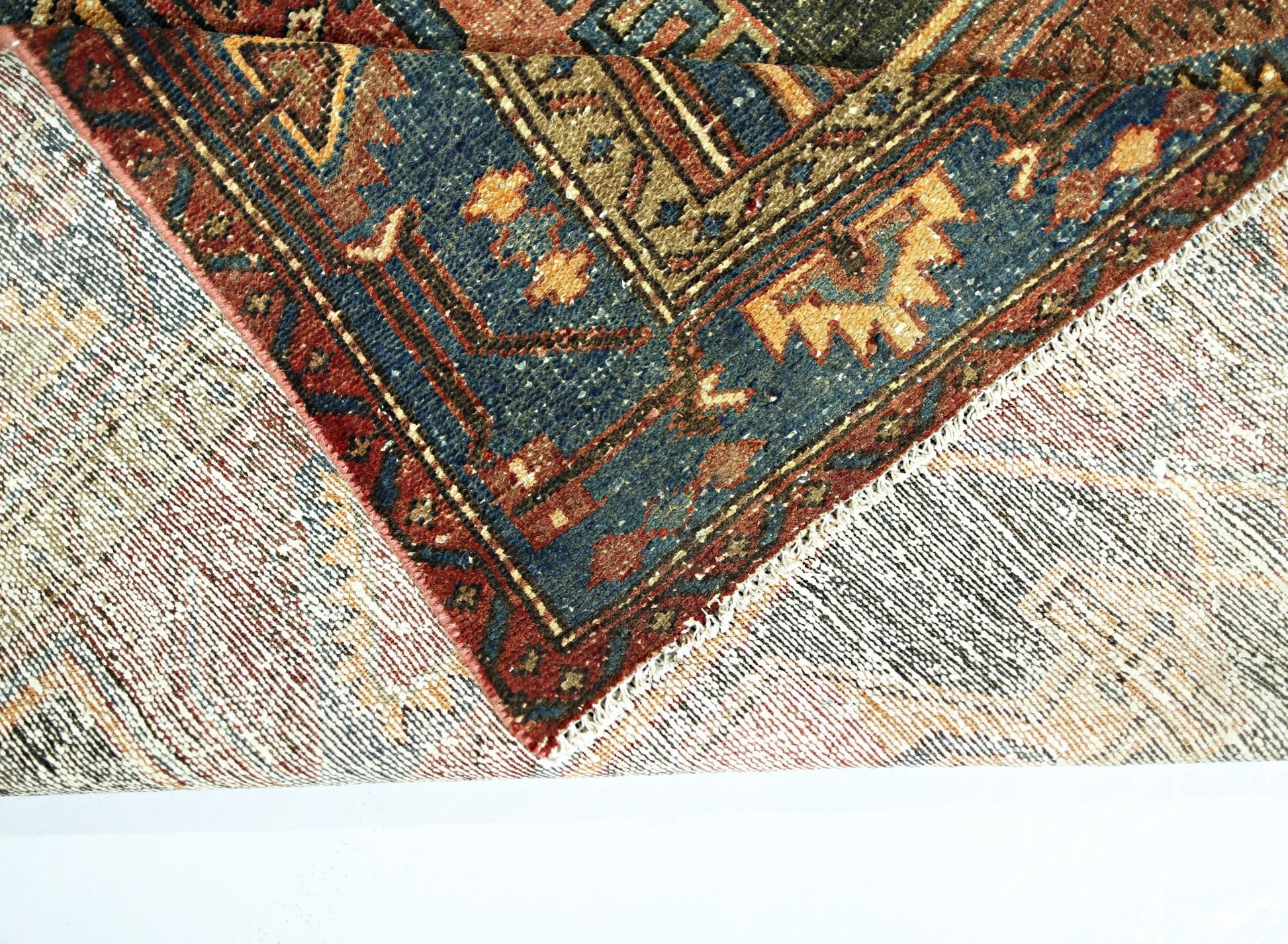 A corner of a vintage Persian rug is folded over to show its intricate blue and red wool pattern.