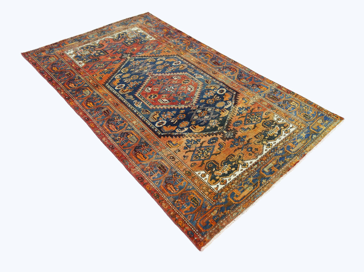 A rectangular vintage Persian rug featuring a central medallion with intricate blue and orange motifs.