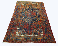 A vintage Persian rug featuring a central blue medallion and intricate geometric patterns in red.