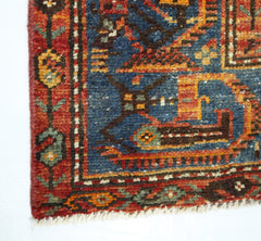 A close-up of a vintage Persian rug featuring intricate geometric patterns in red, blue, and gold.