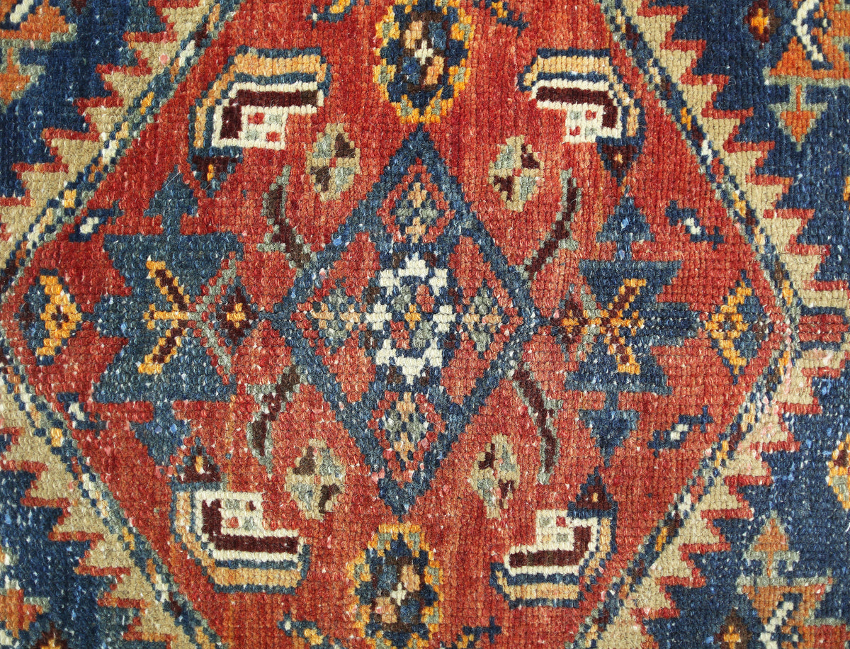 A vintage Persian rug featuring a central geometric diamond motif in red, blue, and cream tones.