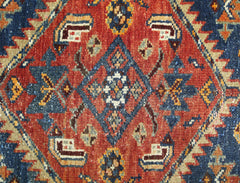 A vintage Persian rug featuring a central geometric diamond motif in red, blue, and cream tones.