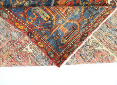 A folded vintage Persian rug featuring intricate geometric patterns in red, blue, and gold tones.