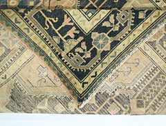 A folded vintage Persian rug featuring intricate floral patterns in black, tan, and muted pink.