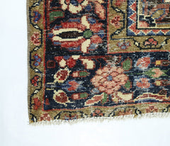 A corner view of a vintage Persian rug featuring intricate floral patterns in red, blue, and gold.