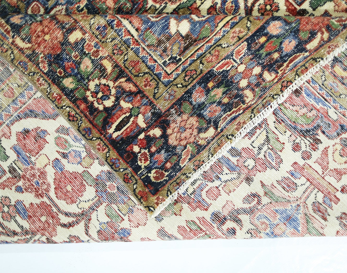 A vintage handmade Persian rug with a floral pattern folded to show its wool pile and cotton base.