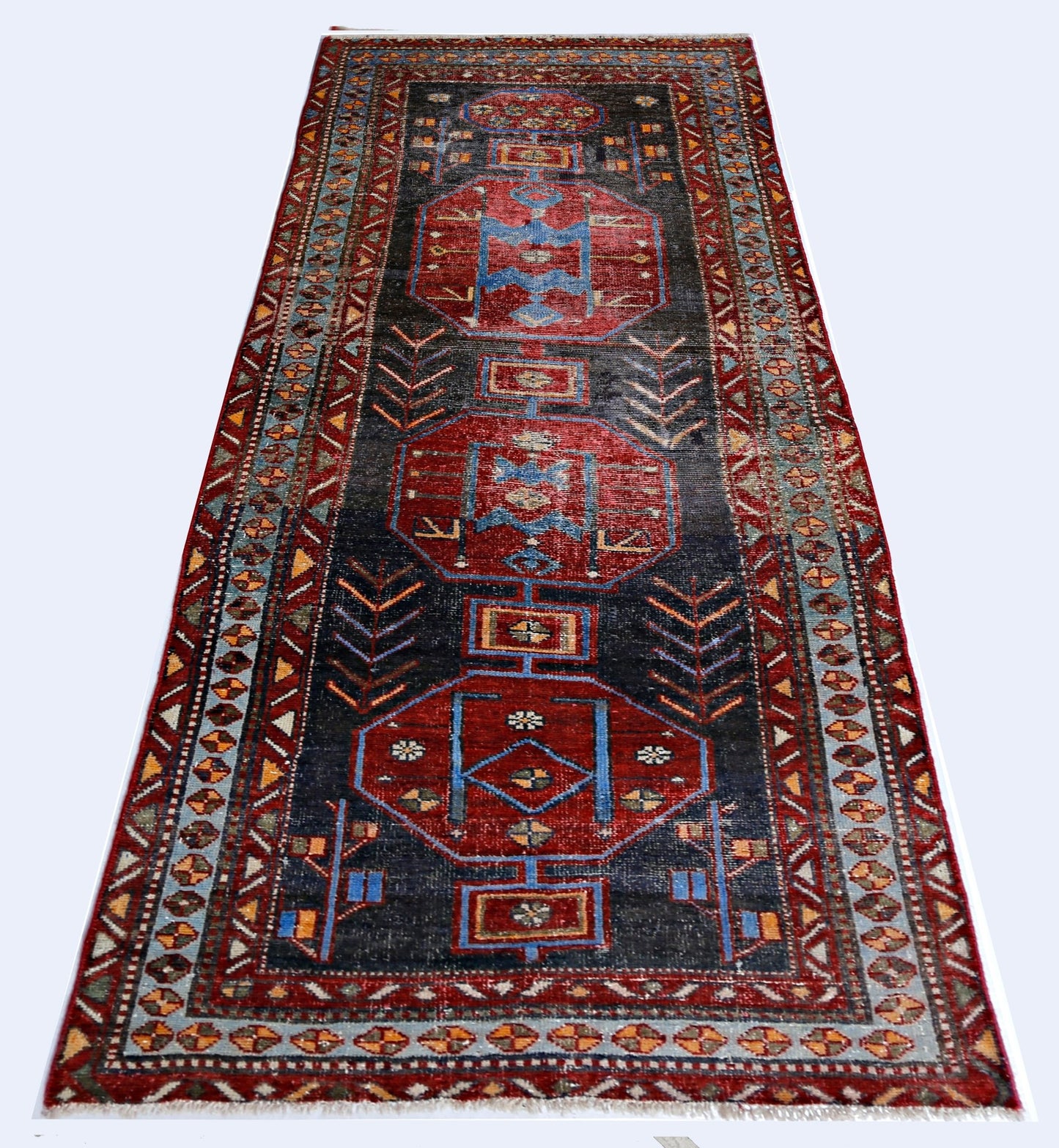 A handmade vintage Persian runner rug featuring geometric medallions in red and blue on a dark field.