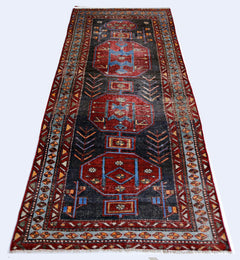 A handmade vintage Persian runner rug featuring geometric medallions in red and blue on a dark field.