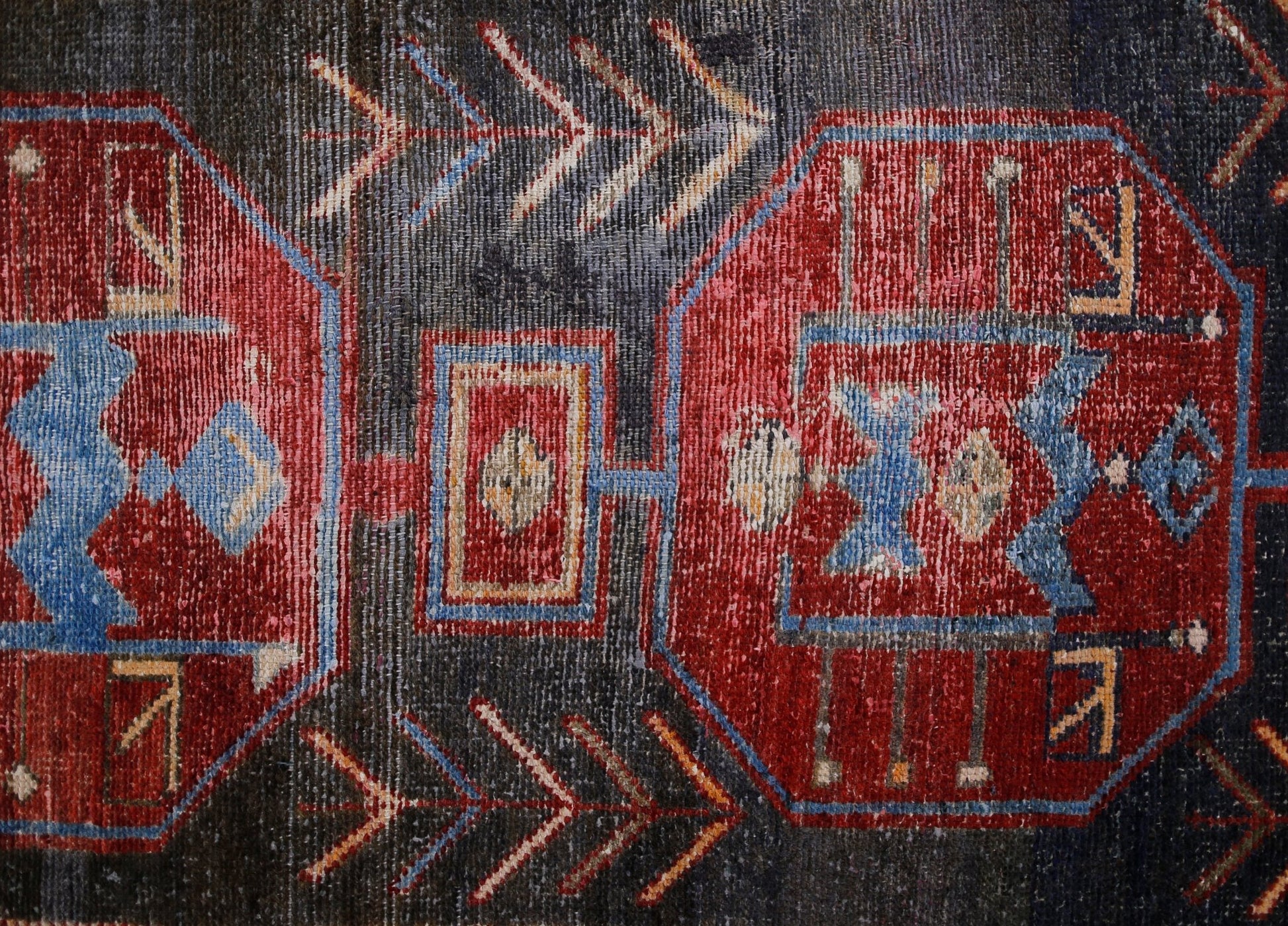 A vintage Persian rug featuring geometric red medallions and arrow motifs on a dark background.