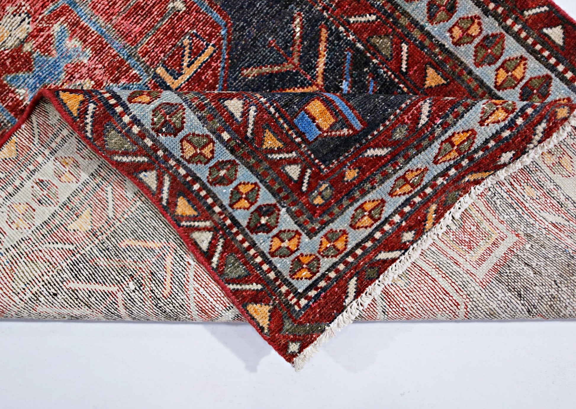 A vintage handmade Persian rug with a geometric pattern in red, blue, and cream wool.