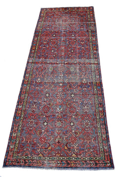 A vintage handmade Persian runner rug featuring a geometric pattern in red, blue, and cream tones.