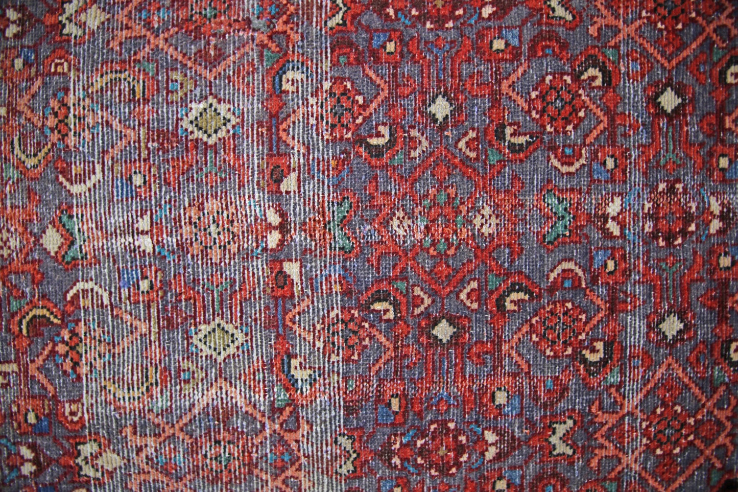 A vintage handmade Persian rug featuring a detailed geometric pattern in red, blue, and cream.