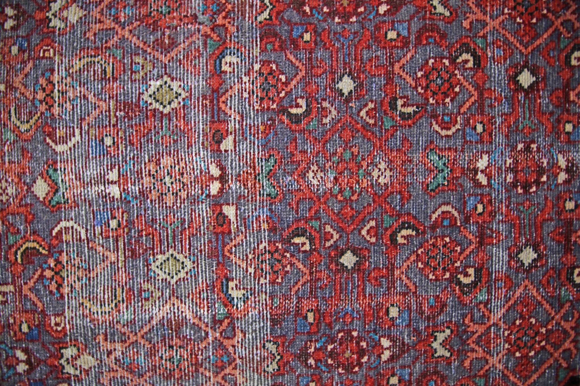 A vintage handmade Persian rug featuring a detailed geometric pattern in red, blue, and cream.