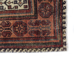 A corner detail of a vintage Persian rug featuring geometric patterns in red, cream, and dark blue.