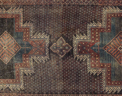 A vintage Persian rug featuring a geometric pattern in deep red, blue, and brown tones.