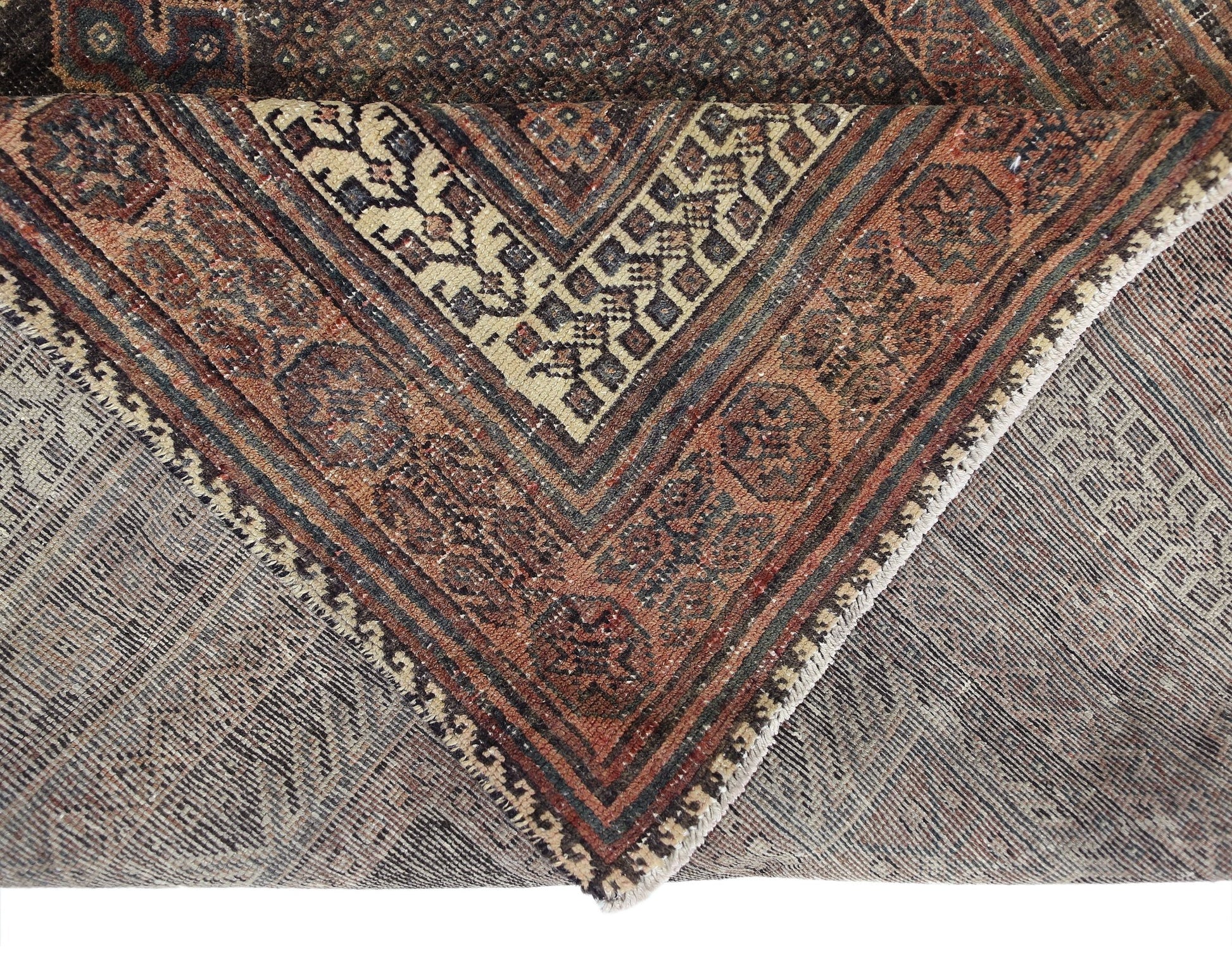 A corner view of a vintage handmade Persian rug featuring geometric patterns in rust and cream.