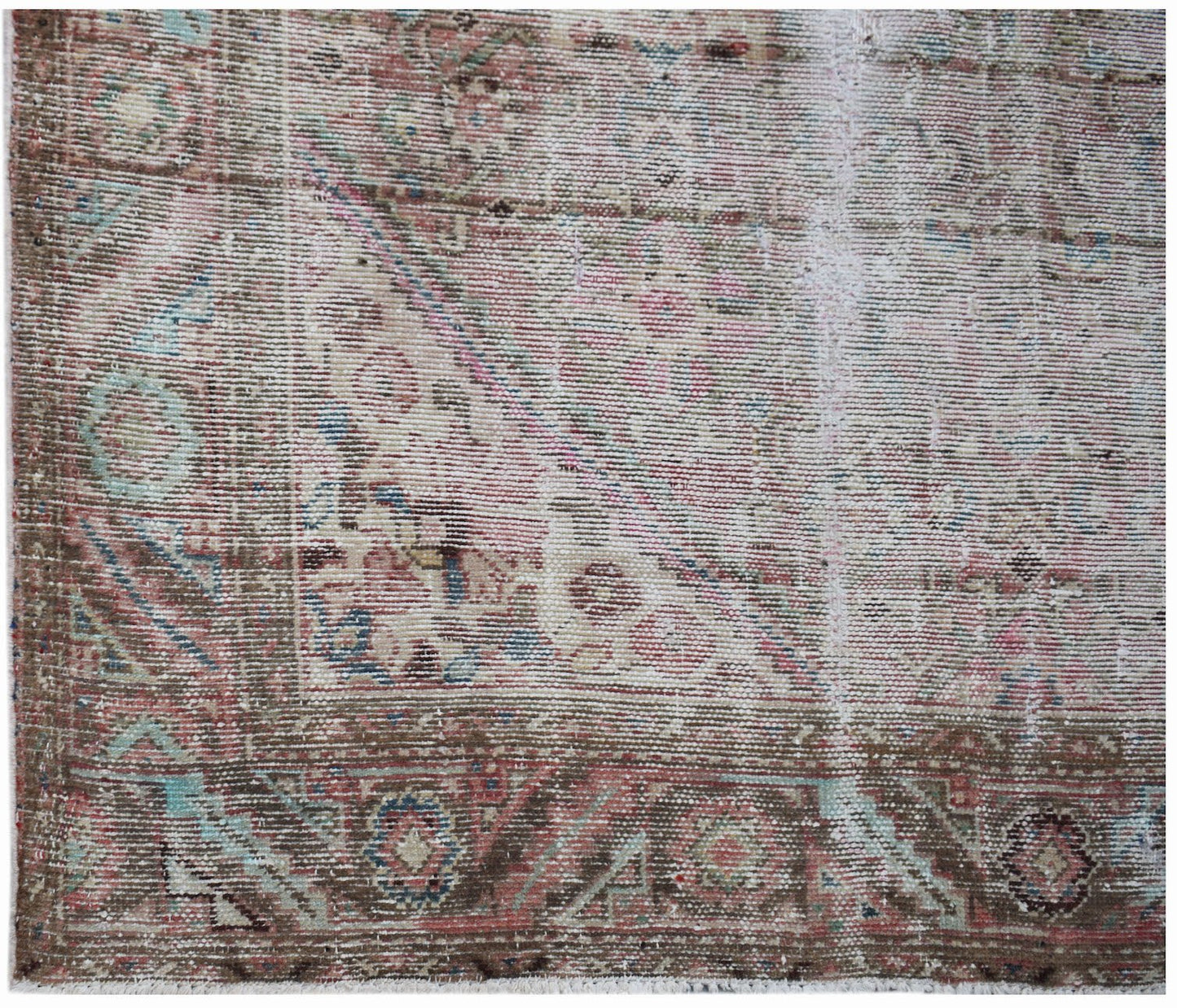 A handwoven vintage Persian rug featuring a faded floral pattern in muted pink, blue, and brown.