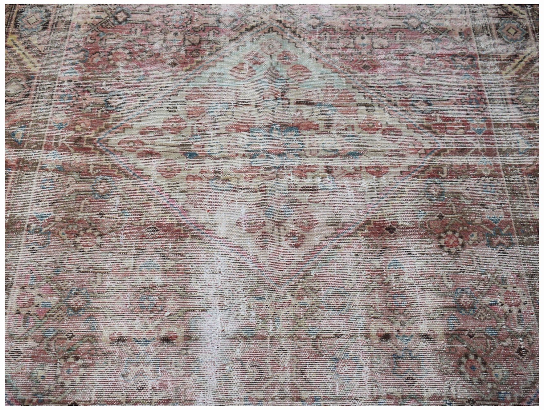 A vintage handwoven Persian rug featuring a faded diamond medallion pattern in muted tones.