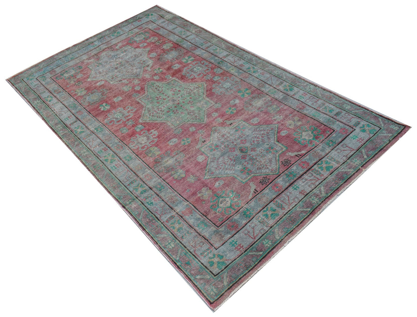 A vintage handwoven Persian rug featuring a faded red field with blue and green geometric motifs.