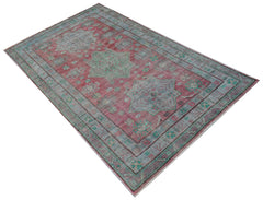 A vintage handwoven Persian rug featuring a faded red field with blue and green geometric motifs.