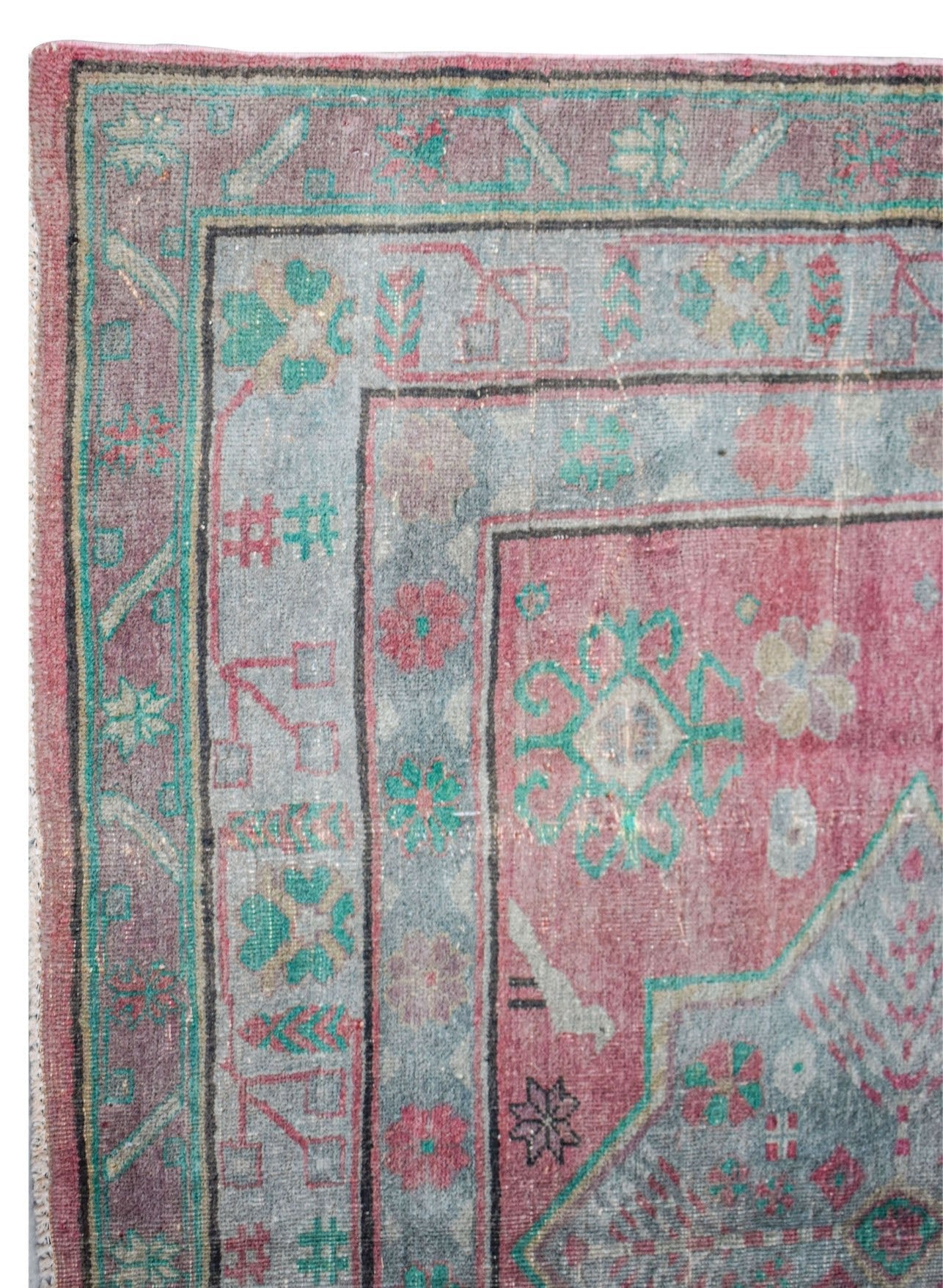 A vintage handwoven Persian rug featuring a faded floral pattern in pink, blue, and green tones.