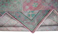 A vintage handwoven Persian rug featuring a faded floral pattern in shades of pink and green.