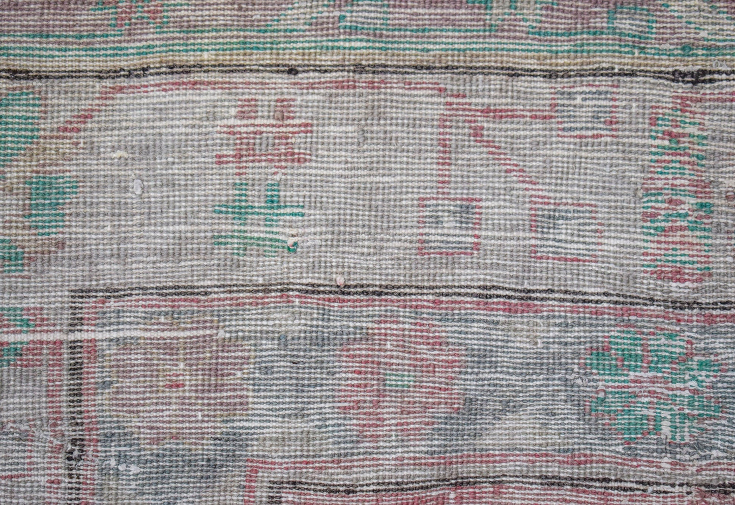 A close-up of a vintage Persian rug featuring faded geometric patterns in red, green, and grey.
